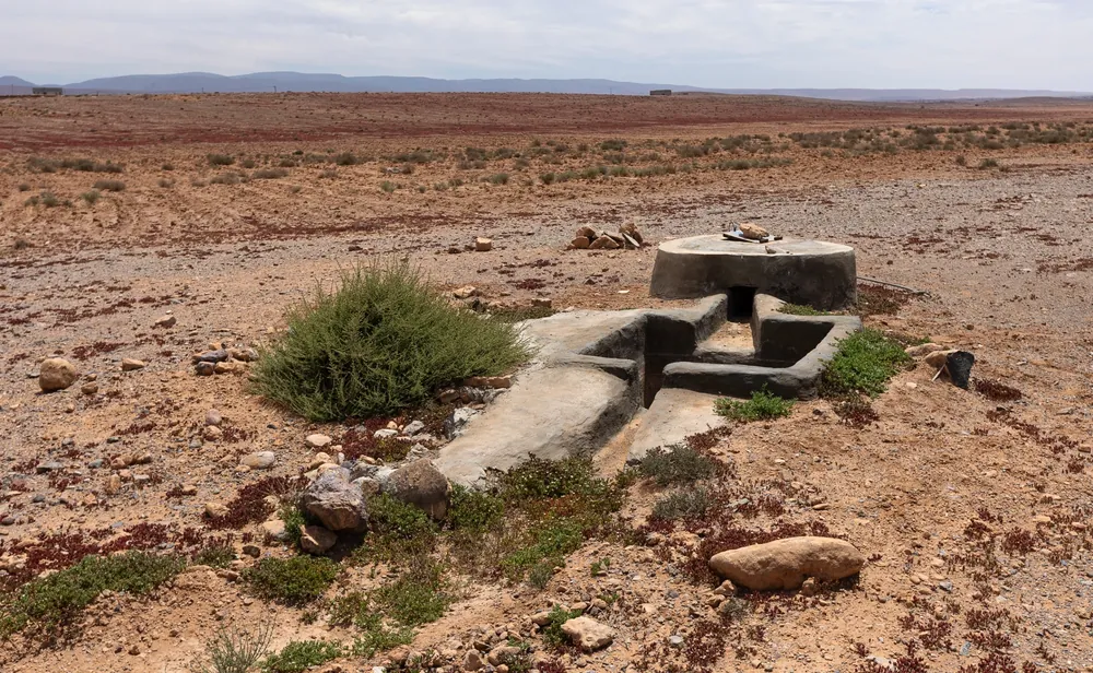 Puits et bassin de captage en béton dans une plaine caillouteuse aride près de Guelmim, Maroc